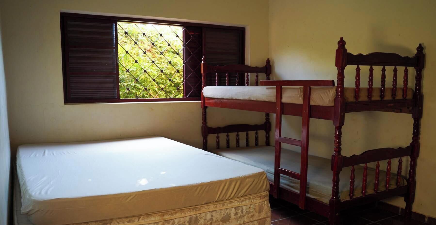 A dormitory room with bunk beds, a single bed, and a window with a view of greenery.