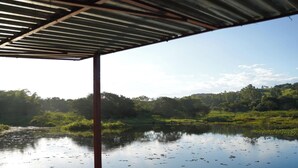 Un espace extérieur abrité offrant une vue sur une étendue d’eau paisible et une colline boisée.