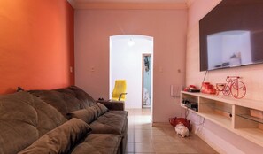 A living room with a brown sofa, a yellow chair, a TV mounted on the wall, and a piggy bank on the floor.