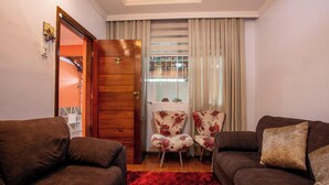 Una sala con dos sofás, una puerta de madera, una ventana con cortinas y un tapete rojo.