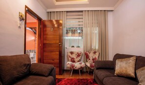 A living room with two sofas, a wooden door, a window with curtains, and a red rug.