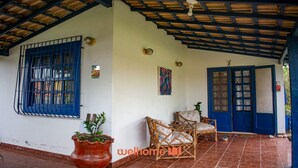Un porche cubierto con piso de baldosas, una puerta azul y una ventana con rejas.