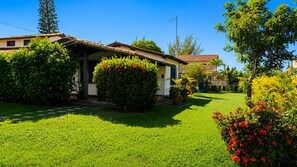 A residential property with a well-maintained lawn, a house with a tiled roof, and various potted plants.
