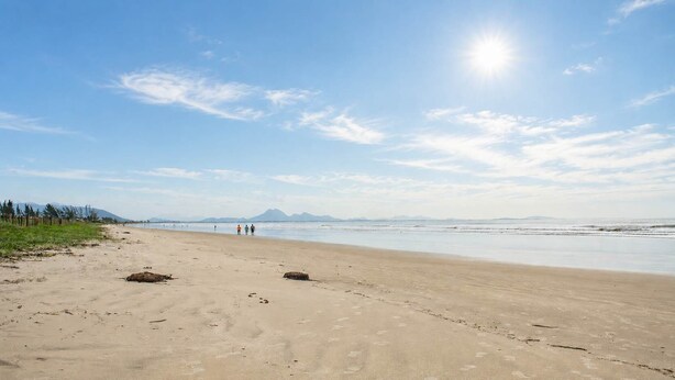 Una playa extensa de arena clara, cielo despejado y montañas a lo lejos.