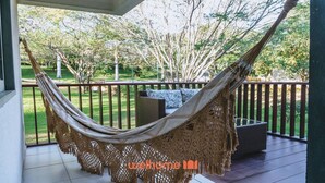 A hammock on a porch with a view of a garden and trees. - Apartamento em Gravatá com Lazer Completo (Gravatá)