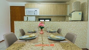 A dining area with a table set for four, a microwave, and a water heater above the counter. - Apartamento em Gravatá com Lazer Completo (Gravatá)