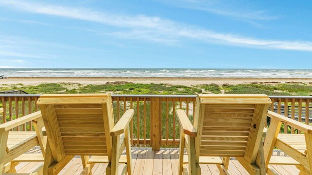 A wooden deck with two chairs facing a beach.