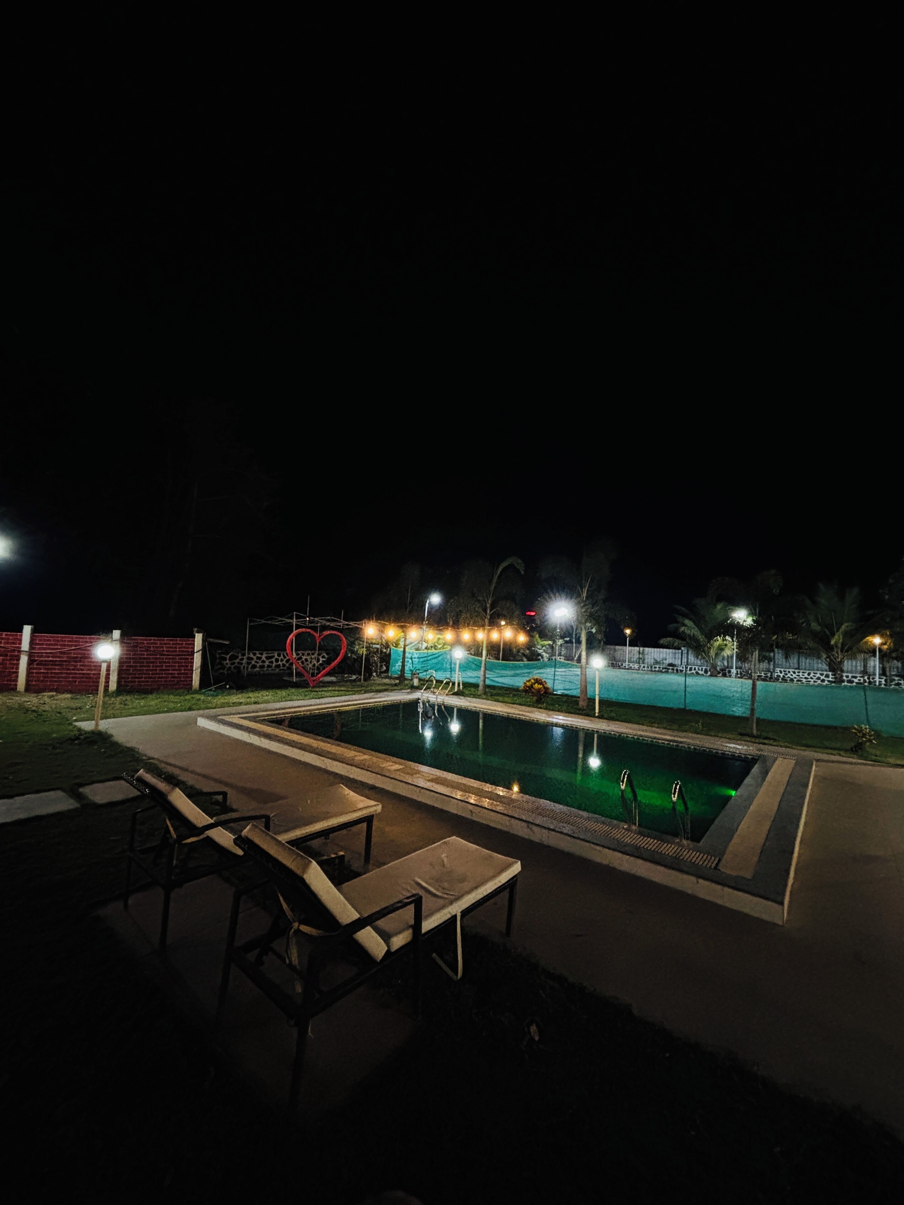 A nighttime pool area with lounge chairs and a heart-shaped decoration.