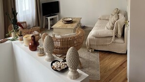 A living room with a high ceiling, a large woven wall hanging, a television, and a cozy seating area with cushions and a rug. - House Bormes village La Valentine, 2 levels, near shops, Air-conditioned (Bormes-les-Mimosas)