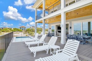 A two-story outdoor deck with white lounge chairs, a pool, and a dining area with tables and chairs.