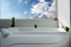 A modern bathroom with a large window, a bathtub, and two potted plants.