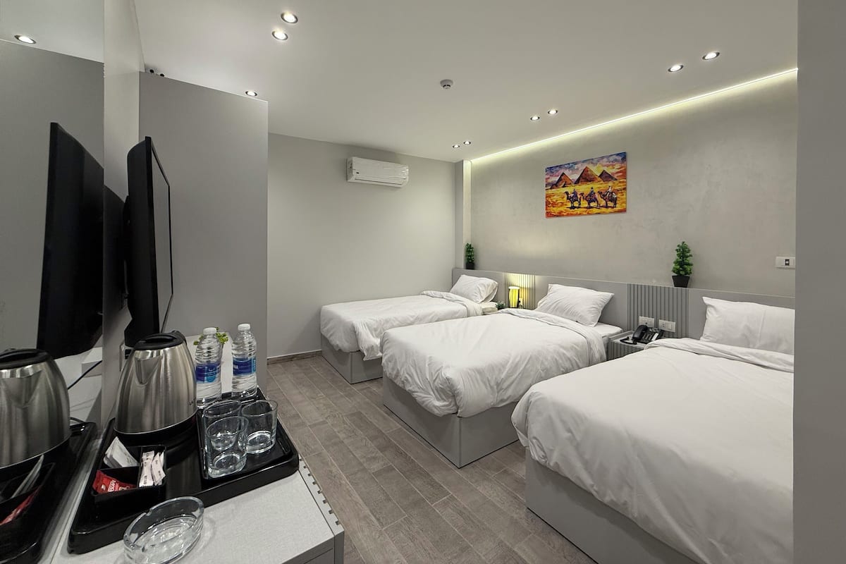 A modern hotel room with two single beds, a flat-screen TV, a coffee maker, and a small table with water bottles and glasses.