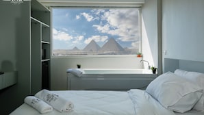 A hotel room with a bed, a window with a view of pyramids, a sink, and a small plant. - Dar Pyramids View Inn RoofTop (Giza)