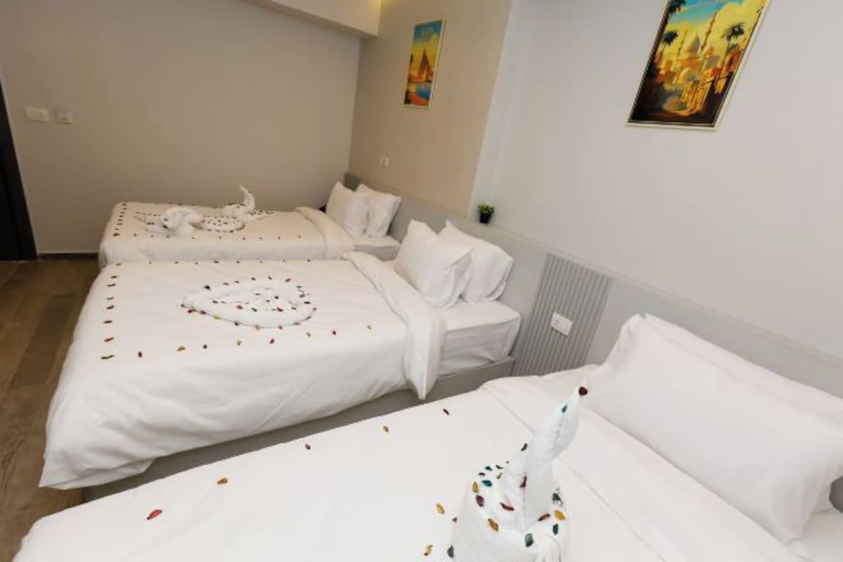 Une chambre d’hôtel avec trois lits alignés, chacun étant doté de draps blancs et de coussins décoratifs.