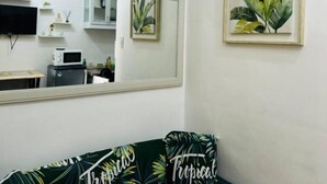 Ein Zimmer mit einem großen Spiegel, einer Uhr, einer gerahmten Zimmerpflanze und einem Sofa mit tropischem Muster.