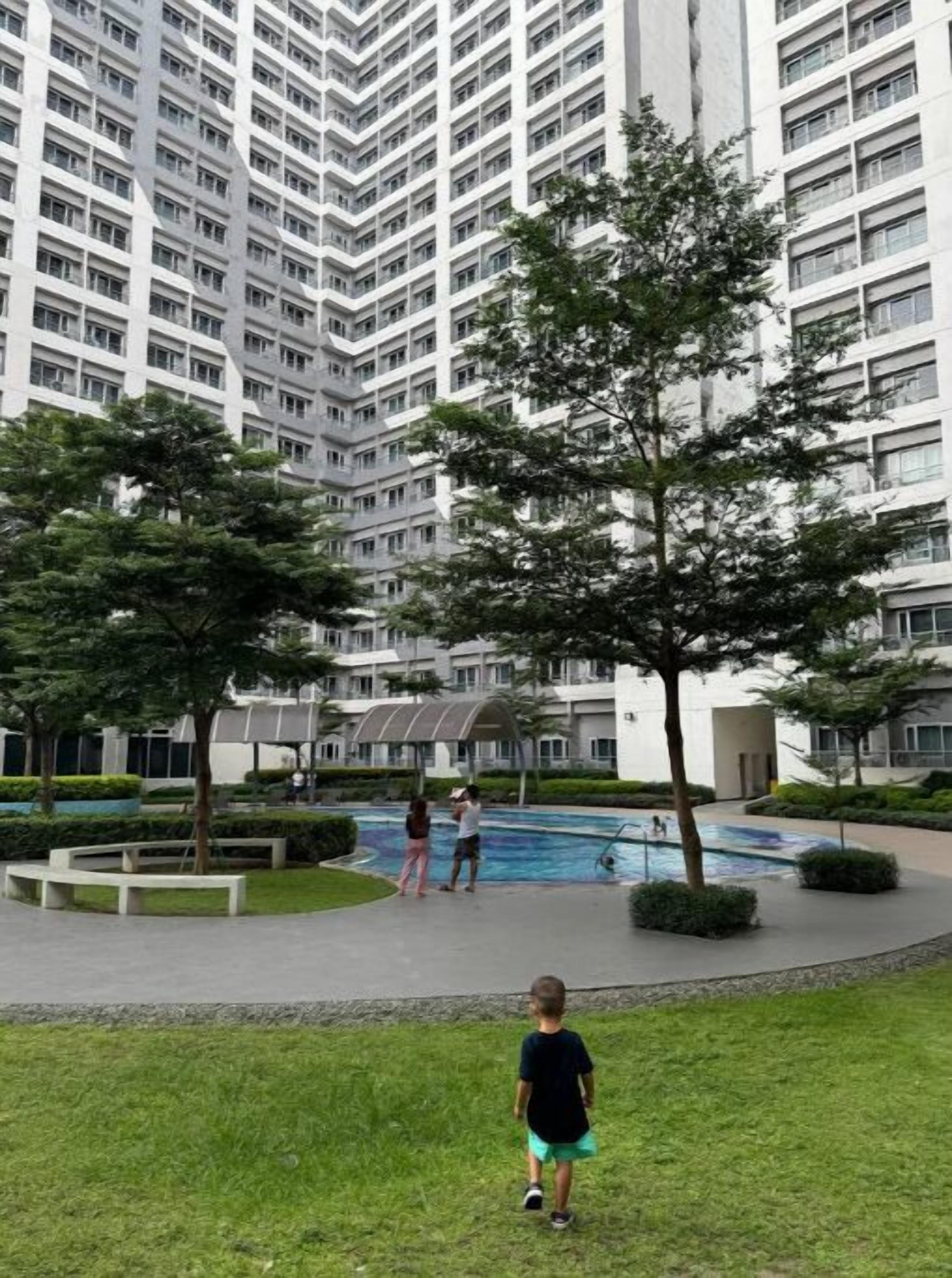 A residential building with multiple balconies, a swimming pool, and a grassy area with trees.