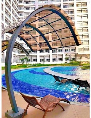 A swimming pool with a curved design, surrounded by a modern building with balconies.