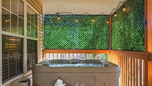 A hot tub with a wooden deck, a glass table with a mug and towels, and a green wall with lights.