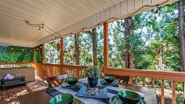 A covered outdoor dining area with a table set for two, surrounded by wooden railings and trees.
