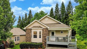 A two-story house with a stone facade, a front porch, and a small garden.