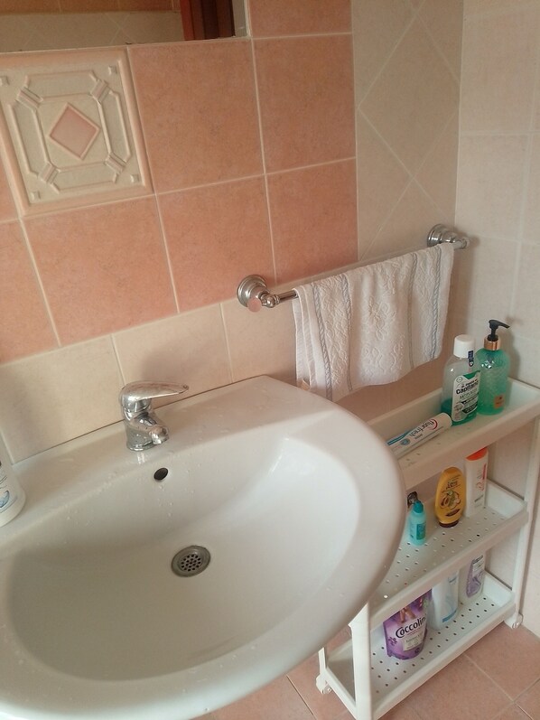 A bathroom with a white sink, a towel rack, and a shelf with toiletries.