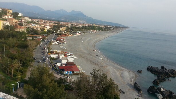 A coastal town with a beach, buildings, and mountains in the background.