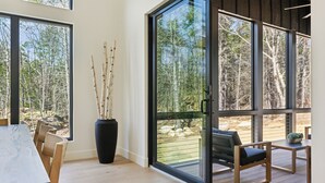 A modern interior with a dining area, a large window with a view of trees, and a sliding glass door leading to an outdoor deck.