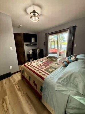 Un dormitorio con cama, ventilador de techo, televisor y ventana con cortinas.