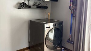 A compact room with a washing machine, a mounted TV, and a vacuum cleaner. - Musky Hideout on Lost Land Lake (Hayward)