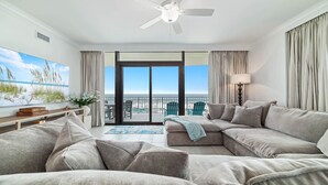 Ett modernt vardagsrum med en stor soffa, ett soffbord och utsikt över stranden genom en skjutdörr i glas.