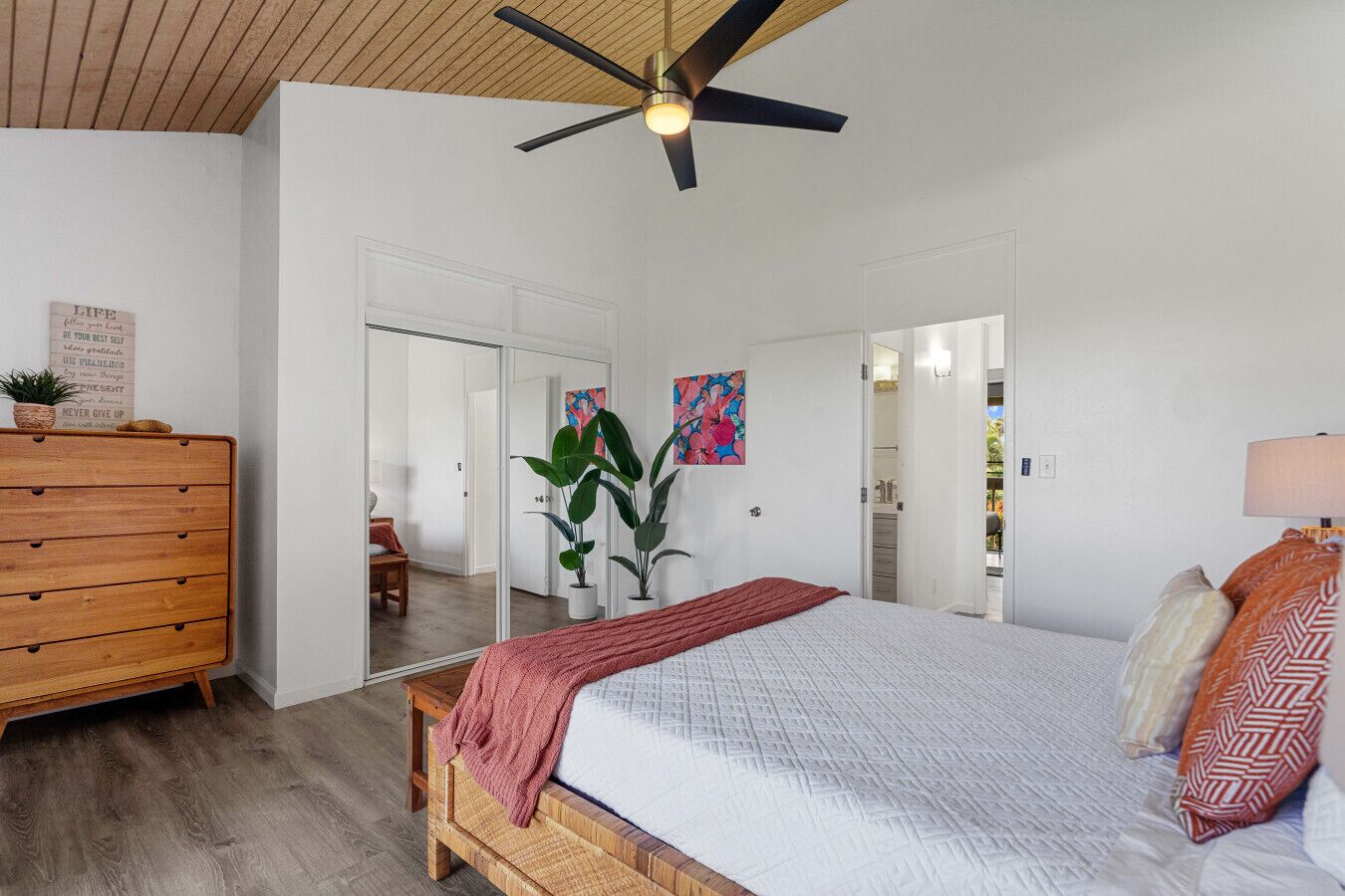 A bedroom with a bed, wooden dresser, ceiling fan, and a large mirror.