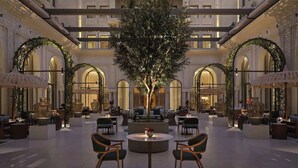Un'ampia hall con un albero centrale, diverse aree salotto e dettagli architettonici ad arco.