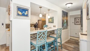 A modern kitchen with white cabinetry, a central island, and a dining area with blue chairs.