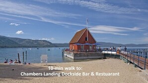 A wooden dockside bar and restaurant with a red building, a pier, and boats on the water.