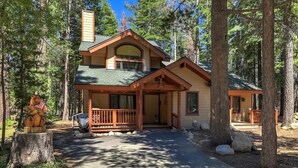 A lodge with a covered porch, a chimney, and a forested backdrop.
