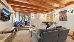 A cozy living room with a grey sofa, wooden ceiling beams, a television, and a painting of a bear.
