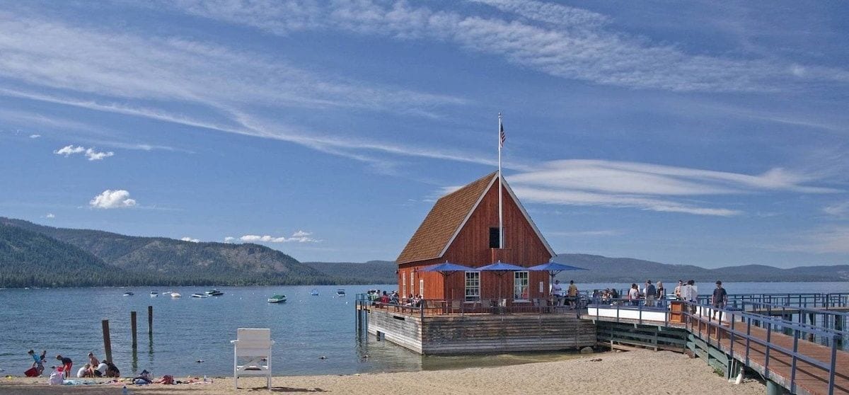 A wooden dockside bar and restaurant with a red building, a pier, and boats on the water.