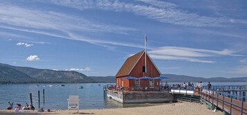 Un bar restaurante de madera junto al muelle, con un edificio rojo, un espigón y barcos en el agua.