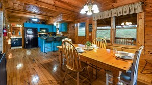 Interior de una cabaña de madera con comedor, cocina y ventanas amplias.