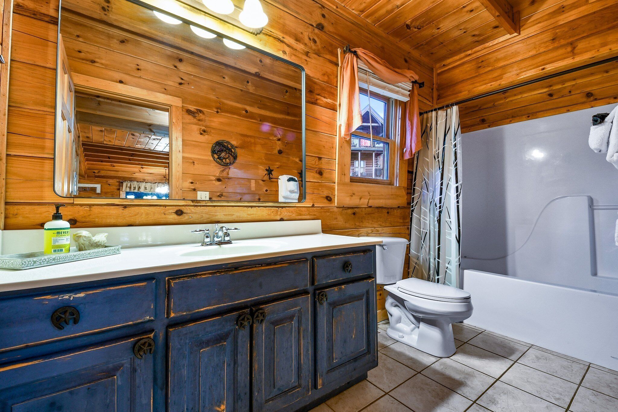 Une salle de bain rustique, avec des murs en bois, un grand miroir, un lavabo blanc et une baignoire.