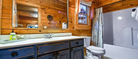 Une salle de bain rustique, avec des murs en bois, un grand miroir, un lavabo blanc et une baignoire.
