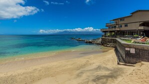 Una playa con agua turquesa cristalina, costa rocosa y un edificio con balcones con vistas al océano.