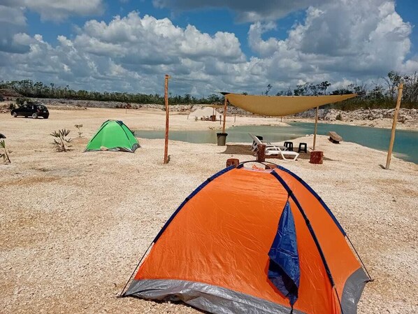 Un camping con tiendas de campaña, una zona con sombra y una playa de arena.