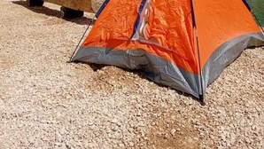 Ett campingtält som är uppställt på en grusstrand, med ett picknickbord i närheten.