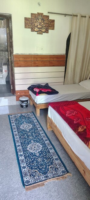 A room with a bed, a wooden headboard, a wall-mounted decoration, a small wooden stool, and a blue patterned rug. - Hotel Kamal Ganga & Restaurant (Rajgarhi)