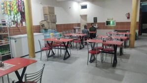A restaurant with multiple tables and chairs, a refrigerator, and a tiled wall. - Hotel Kamal Ganga & Restaurant (Rajgarhi)