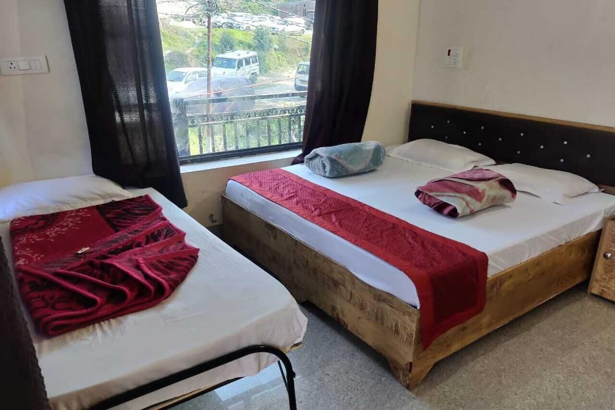 A room with two single beds, each with a red blanket and a pillow. There is a window with a view of parked cars outside.