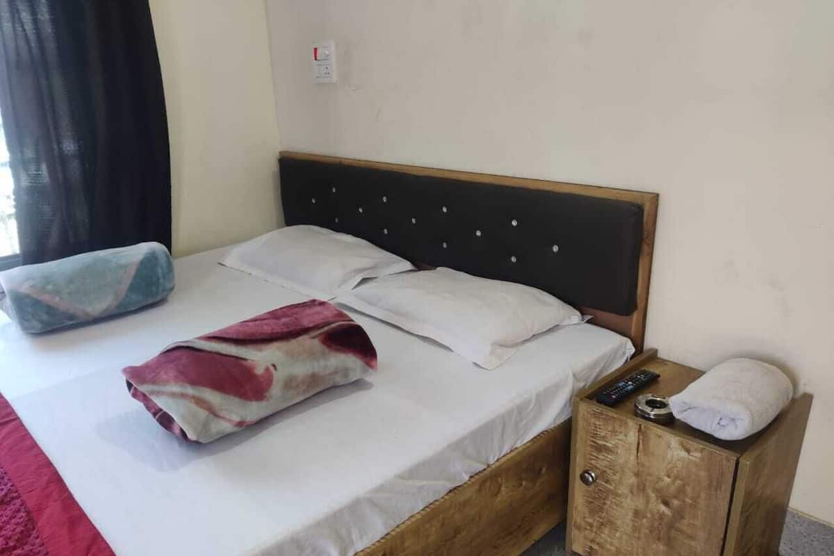 A single bed with a wooden headboard, a bedside table with a remote control, and a small wooden cabinet.