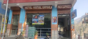 A hotel named "Hotel Kamal Ganga & Resturant" with a glass facade and multiple posters advertising local attractions. - Hotel Kamal Ganga & Restaurant (Rajgarhi)