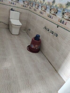 A bathroom with a toilet, a red water heater, and a shower with a glass door. - Hotel Kamal Ganga & Restaurant (Rajgarhi)